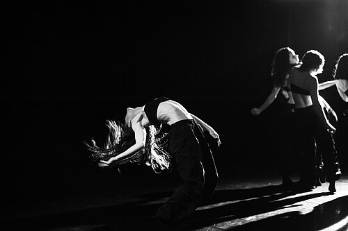 Schwarz-Weiß-Fotografie von vier Tänzerinnen, die Bühne ist dunkel