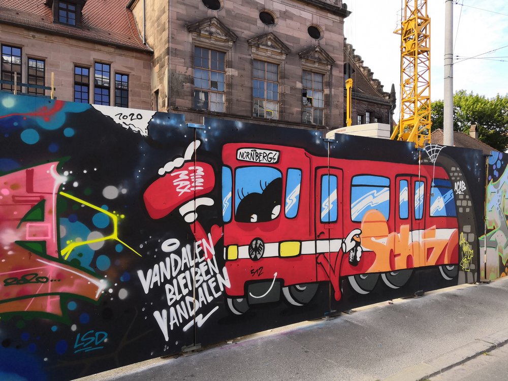 Graffiti-Kunst am Bauzaun entlang des Königstorgraben: Eine typische Nürnberger U-Bahn und das Statement "Vandalen bleiben Vandalen"