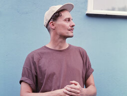 Vincent von Flieger mit Cap und T-Shirt vor einer blauen Hauswand