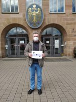 Mann mit Maske vor Rathaus mit Plakat