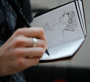 Das Foto zeigt eine Hand, die ein Portrait in ein Skizzenbuch zeichnet