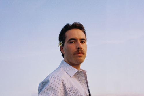 Portraifoto eines Mannes mit hellem Hems, im Hintergrund blauer Himmel