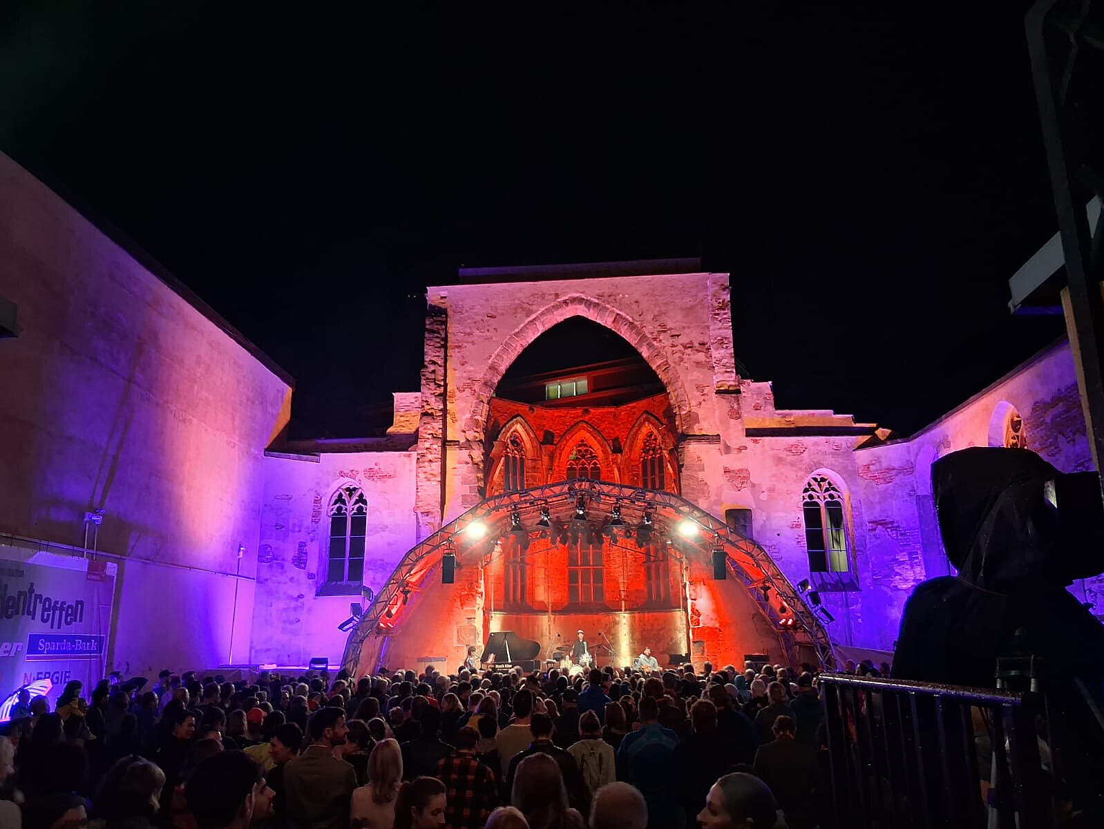 Große Menschenmenge vor einer beleuchteten historischen Backsteinfassade mit roter und violetter Bühnenbeleuchtung bei Nacht