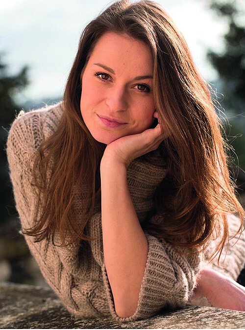 Frau mit langen brauen Haaren stützt ihr Gesicht mit der Hand 