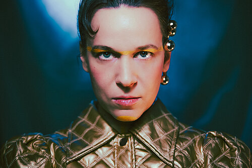 eine Frau mit glänzender Jacke, die Haare nach hinten gebunden