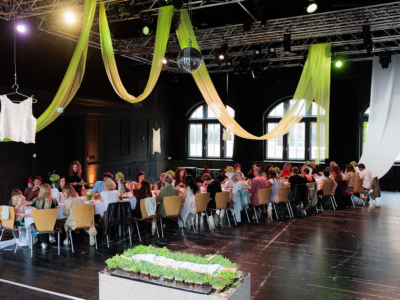 Eine lange Tafel, an dem viele Menschen sitzen steht im Festsaal des Künstlerhauses.