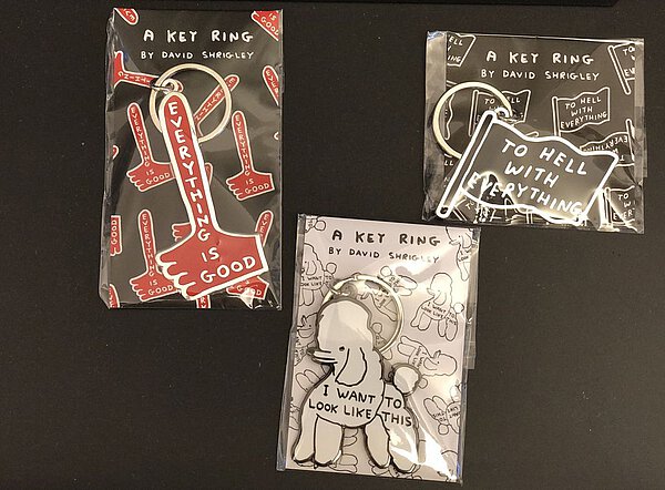 Drei Schlüsselanhänger von David Shrigley: eine Fahne mit Aufdruck To Hell With Everything; ein weißer Pudel mit Aufdruck I Want to Look Like This und ein roter Hammer mit Aufdruck Everything is Good