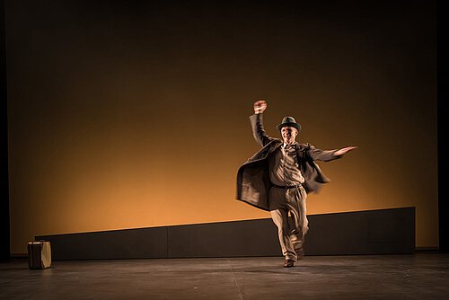 Ein Mann mit Mantel und Hut in einer stürmischen Bewegung.