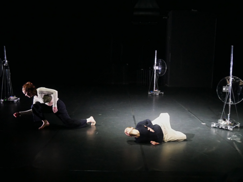 zwei Performerinnen und zwei Roboter gemeinsam auf einer schwarzen Bühne