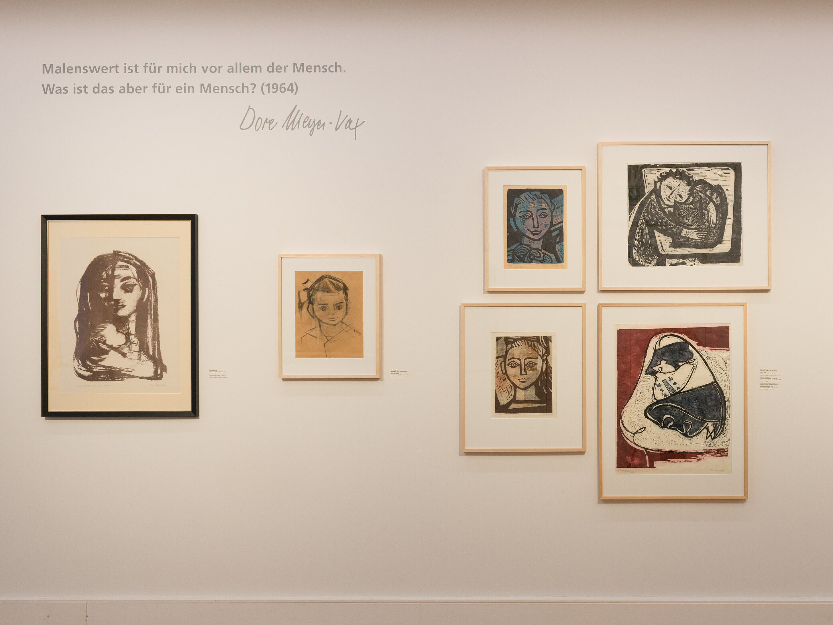 Die Künstlerin Dore-Meyer Vax präsentiert mehrere Werke auf einer Wand: Dore Meyer-Vax, Die Mutter (Junge Mutter), 1959, Lithografie auf Papier, 76 x 54 cm, Privatsammlung; Asti, um 1958/59, Kohlezeichnung auf Papier, 37 x 29 cm, Privatsammlung; Junge, 1960, Linolschnitt auf Papier, 41 x 30 cm, Sammlung Matthes; Kind mit Katze, 1967, Linolschnitt auf Papier, 51 x 59 cm, Sammlung Kunstvilla; Junge, um 1960, Linolschnitt auf Papier, 50 x 40 cm, Sammlung Sauer; Ruhendes Mädchen, 1952, Linolschnitt auf Papier, 67 x 54 cm, Sammlung Matthes; Freundinnen, 1950, Öl auf Leinwand, 60 x 70,5 cm, Sammlung Kunstvilla; Krankes Mädchen im Bett, 1948, Öl auf Leinwand auf Karton, 50 x 70 cm; Mädchen im Sessel, 1949, Öl auf Leinwand, 60 x 50 cm, (von links nach rechts) Foto: © Kunstvilla, Annette Kradisch  