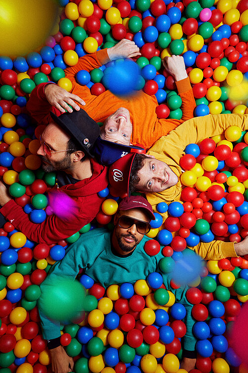 vier Männer mit bunten Pullis in einem Bällebad