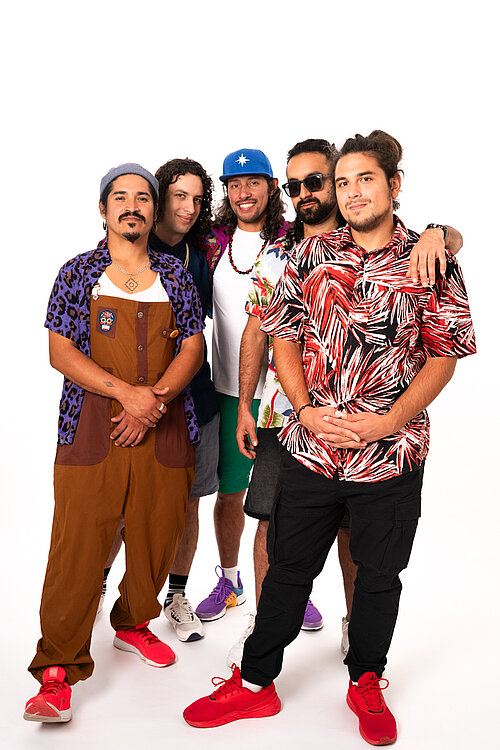 die fünf Bandmitglieder vor einem weißen Hintergrund, alle schauen in die Kamera, sie tragen unterschiedliche teilweise bunte Kleidung