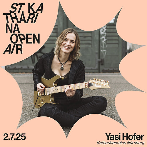 Eine Frau in schwarzer Kleidung sitzt auf dem Boden und spielt E-Gitarre, sie lächelt dabei