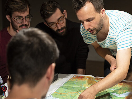 mehrere Menschen sitzen um einen Tisch, auf dem Tisch liegt eine Landkarte