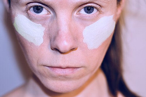 Frauengesicht mit blauen Augen und weißer Bemalung auf den Wangen