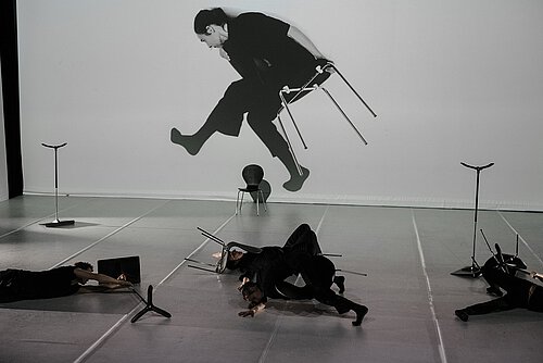 Tänzer liegen auf der Bühne , auf der Leinwand im Hintergrund Mensch auf fliegendem Stuhl