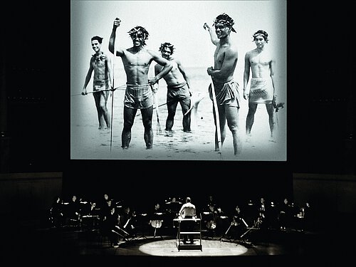 Leinwand mit SchwarzweißFilm, davor eine Bühne