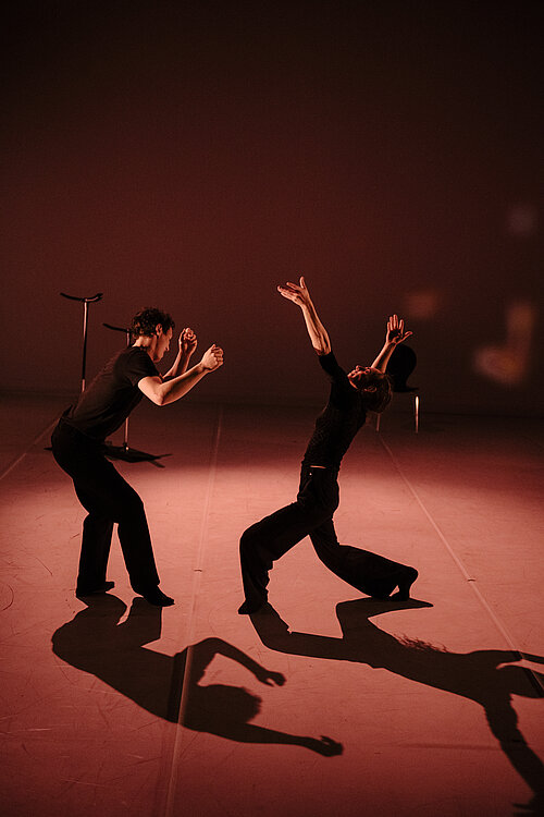 zwei Menschen schwarz gekleidet in Pose auf der Bühne in rotem Scheinwerferlicht