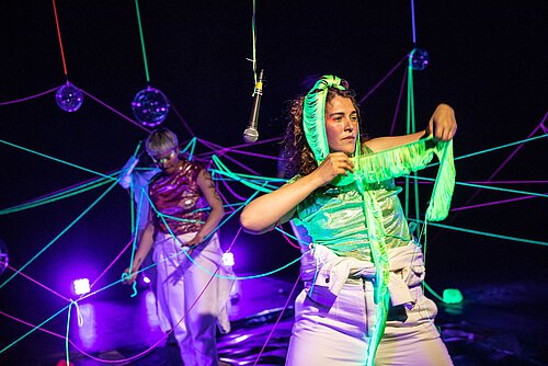 zwei Frauen in neonfarbenen Bändern verstrickt