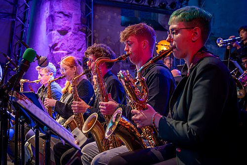 Fünf MusikerInnen spielen Saxophon auf einer Bühne.
