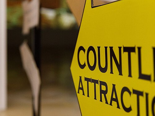 Ein großer gelber Pfeil bewirbt mit schwarzer Schrift die Ausstellung als Attraktion