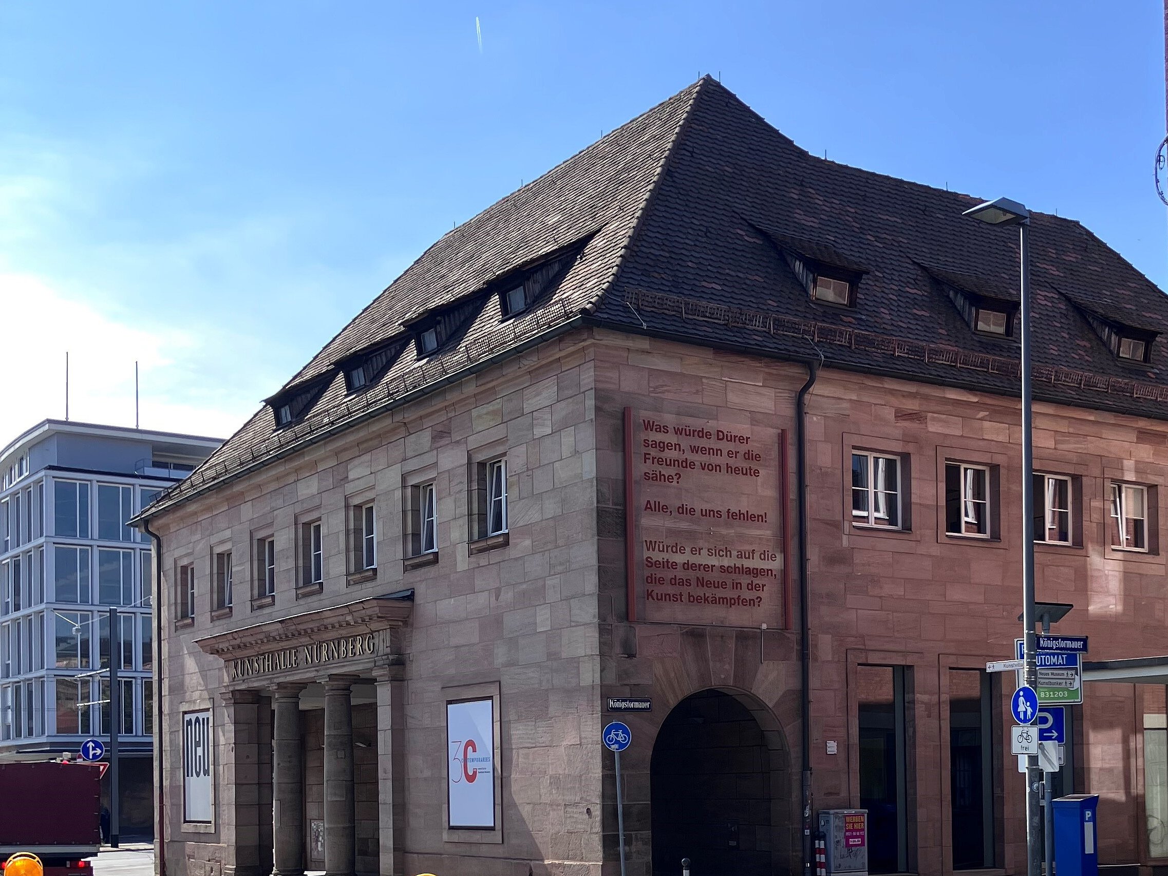Steinernes historisches Gebäude mit Arkaden und großen Bannern. Auf einem Banner steht ein Text in roten Buchstaben.
