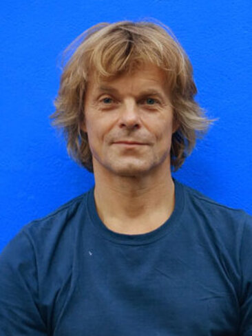 Ein Portrait von Henrik Kaalund in blauem T-Shirt vor blauem Hintergrund