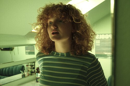 junge Frau mit kurzen roten lockigen Haaren in grünem Licht