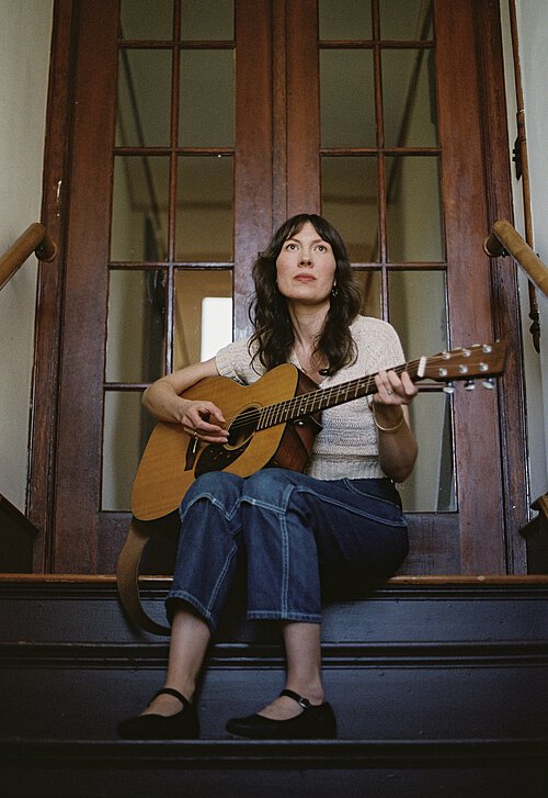 Eine Frau sitzt auf einer Treppenstufe mit einer Gitarre