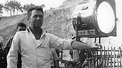 Alfred Vohrer steht an einem Filmset vor einem großen Scheinwerfer