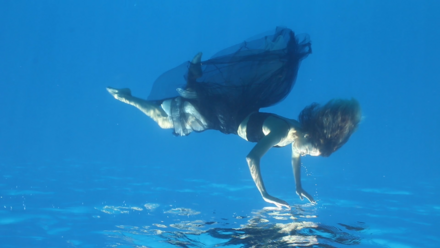 Ein Frau in Kleid taucht in blaues Wasser ein.