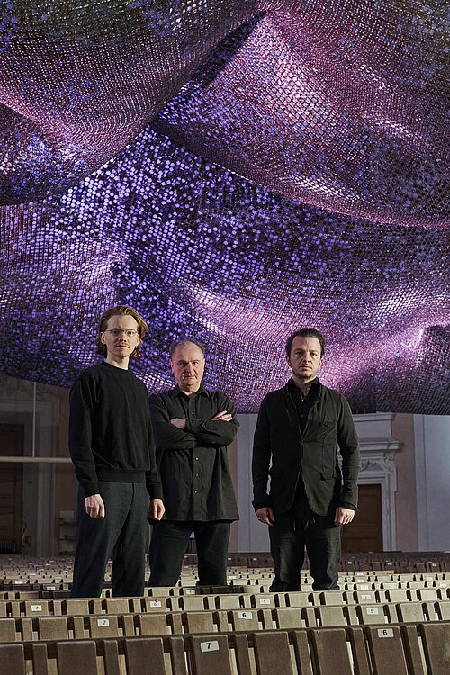 drei Männer in schwarz gekleidet in leerem Stuhlraum