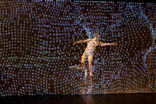 Der Tänzer Henrik Kaalund breitet beide Arme aus und schwebt durch einen Wald aus Buchstaben. 