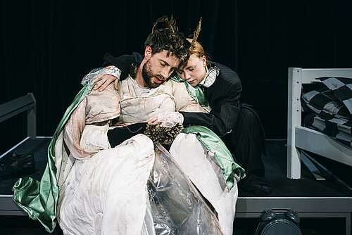 Mann in Käferkostüm und Frau in Anzug sitzen, sich umarmend