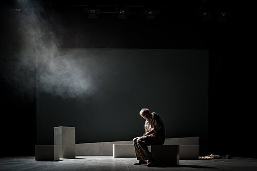ein Mann sitzt zusammengesunken auf einem Block in einem abgedunkelten Raum