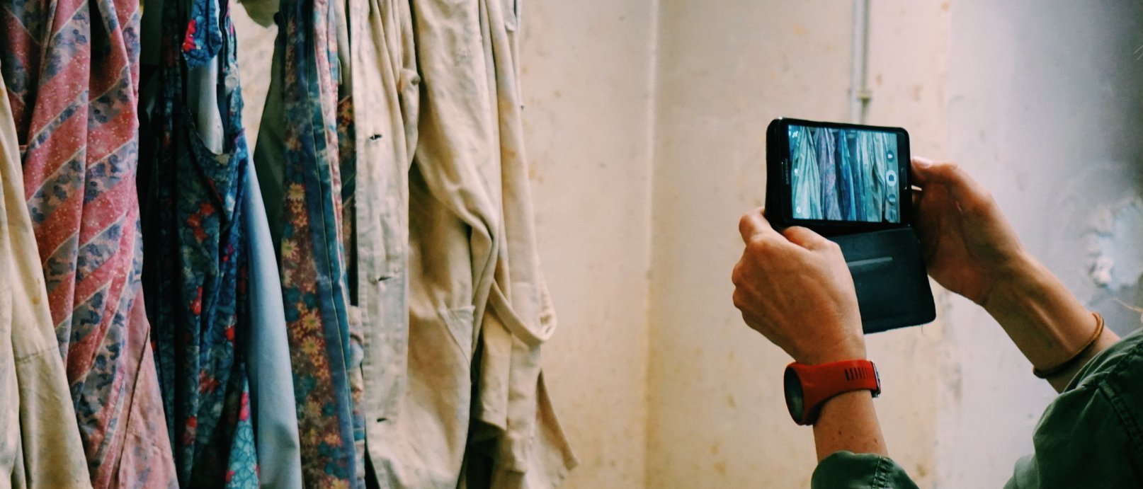 Person fotografiert mit Smartphone an einer Garderobe aufgehängte Kleidungsstücke