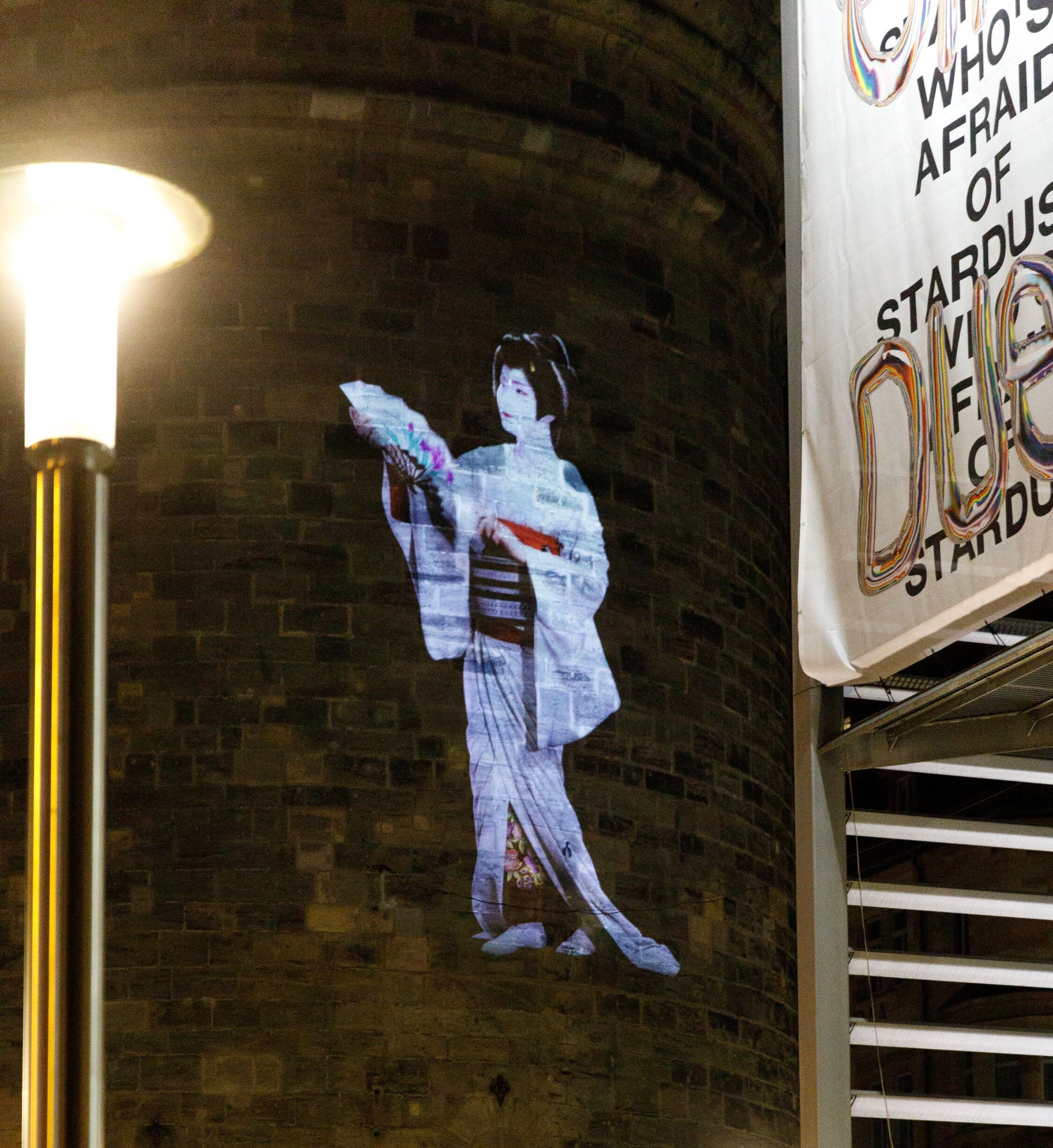 Die überlebensgroße Projektion zeigt die Verwandlung der einzigen männlichen Geisha Japans von einem Mann in eine Geisha