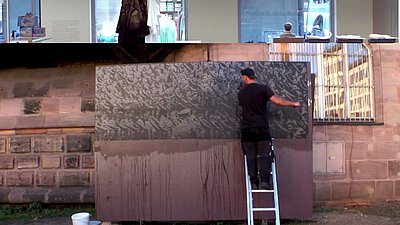 Eine große Cortenstahlplatte wird mit einer Schwarzweißfotografie, die die Hitlerjugend während eines Reichsparteitagsgeländes zeigt