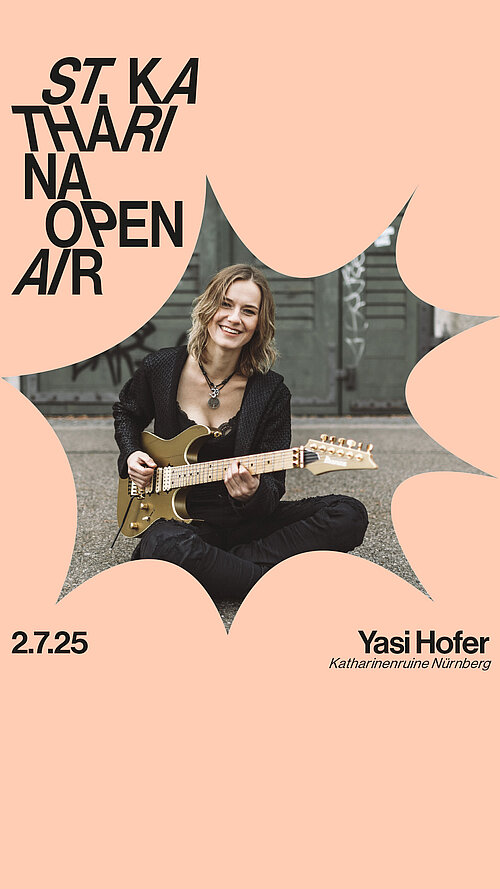 Eine Frau in schwarzer Kleidung sitzt auf dem Boden und spielt E-Gitarre, sie lächelt dabei