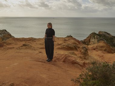 junge Frau, schwarz gekleidet auf Felsen vor dem Meer