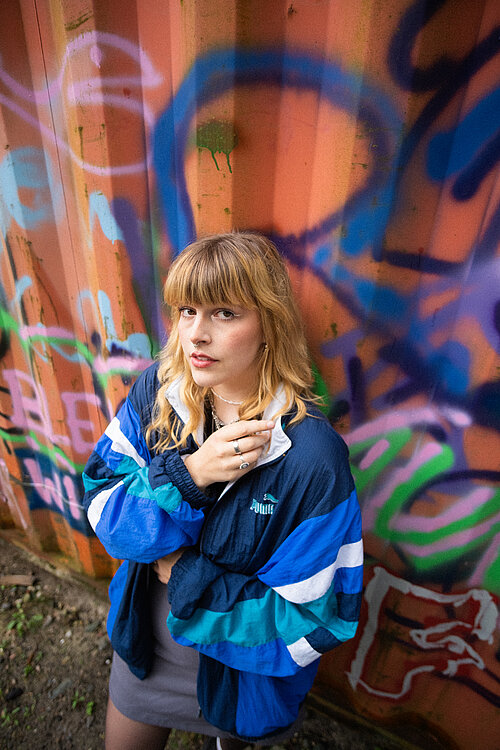 eine junge Frau vor einem bunt angesprühten Container