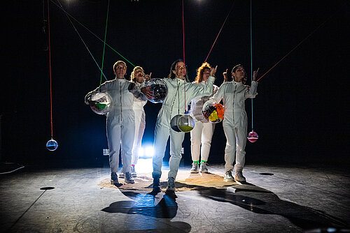 fünf Frauen in weißen Overalls auf der belichteten Bühne