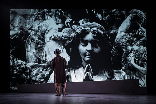 ein Mann steht vor einer Projektion von einem steinernen Engel