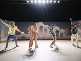 Schauspieler und Tänzer tanzen in bunter Kleidung auf der Bühne