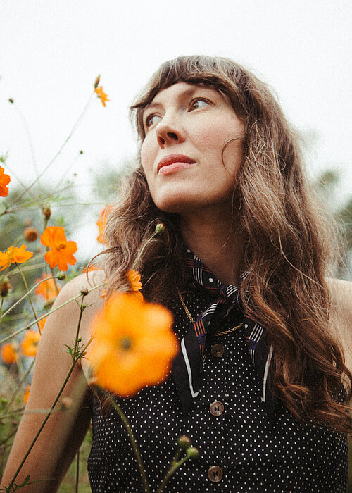 Eine Frau mit braunen langen Haaren steht in einem Blumenfeld