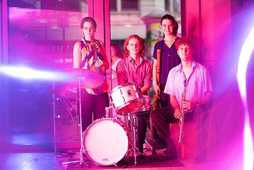 Vier junge Musiker:innen mit ihren Instrumenten durch Pink-Filter fotografiert