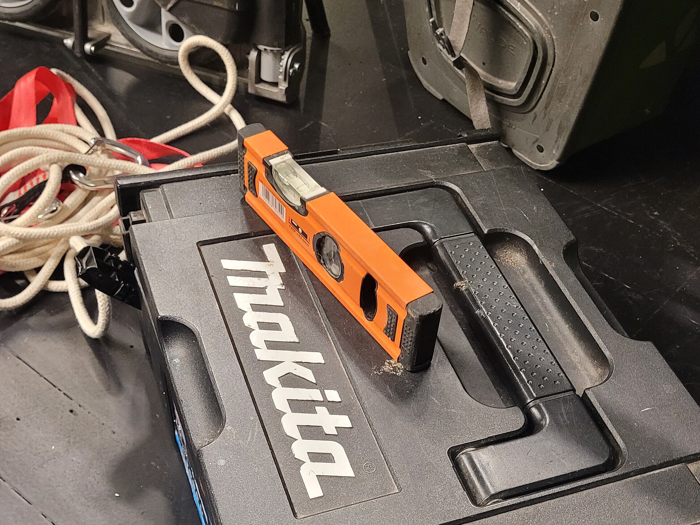 Schwarzer Makita-Koffer mit weißem Logo, darauf liegender oranger Wasserwaage mit zwei Libellen, im Hintergrund Kabel und Werkzeugkoffer.