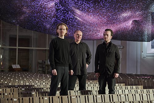 drei Männer in schwarz gekleidet in leerem Stuhlraum