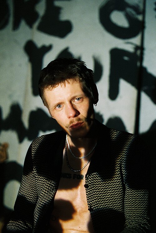 ein Mann blickt in die Kamera, ein paar Schatten fallen auf ihn