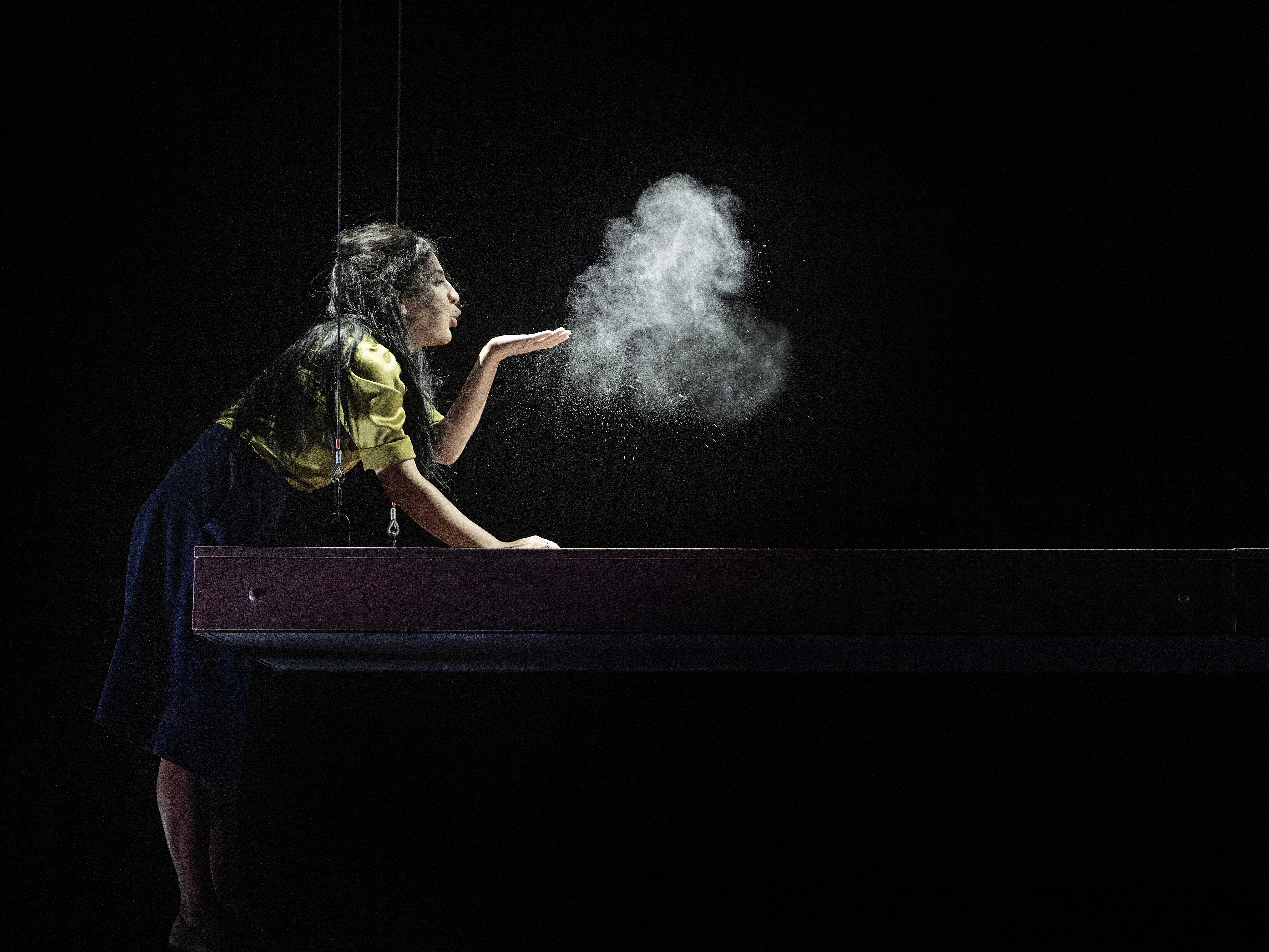 Frau lehnt sich über einen Billardtisch und bläst eine Wolke aus weißem Pulver in die Luft vor schwarzem Hintergrund.